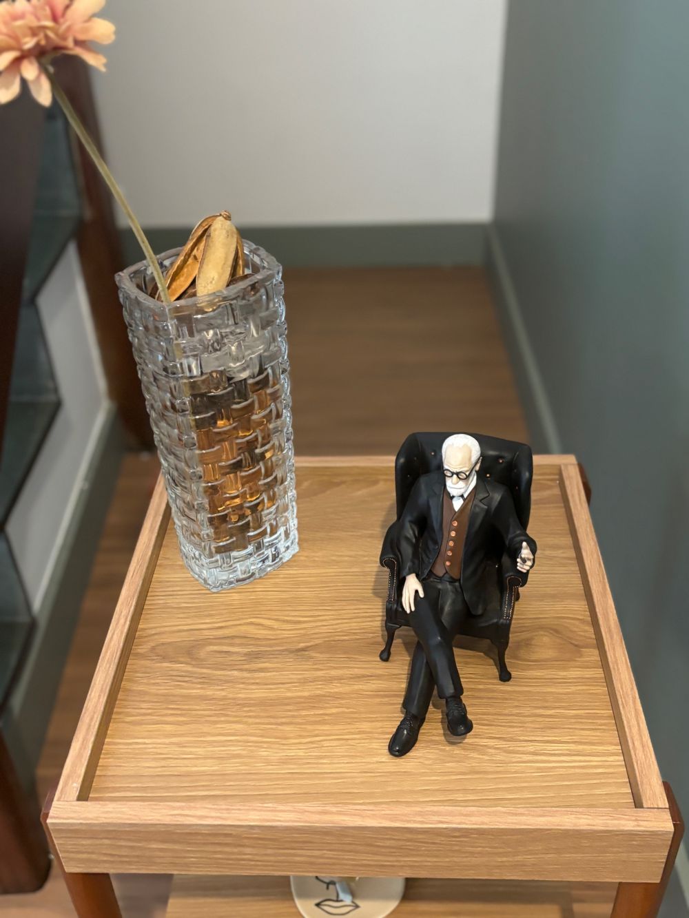 Miniatura de Freud na poltrona sobre uma mesa de madeira, ao lado de um vaso de vidro
