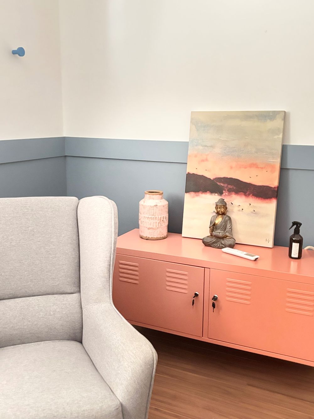 Consultório com poltrona cinza, aparador coral e parede azul