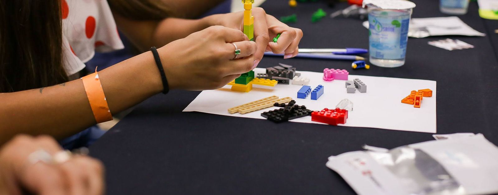 Mãos de participantes construindo lado a lado na mesa